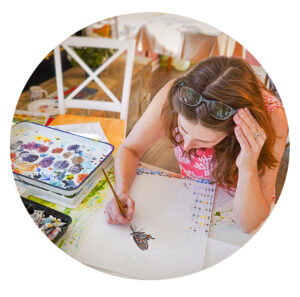Overhead shot of Sketch Club co-founder Cordelia Norris painting a butterfly in watercolor